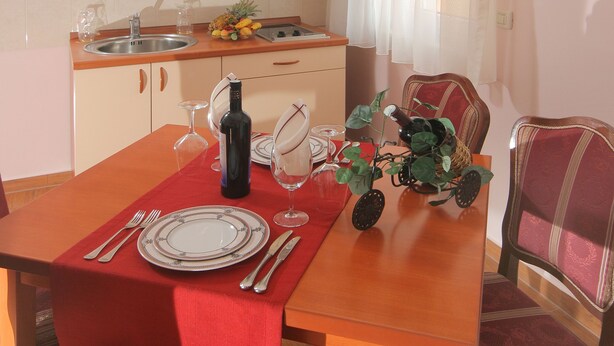 Un comedor con una mesa de madera dispuesta para cuatro, una cocina al fondo y una ventana con cortinas.