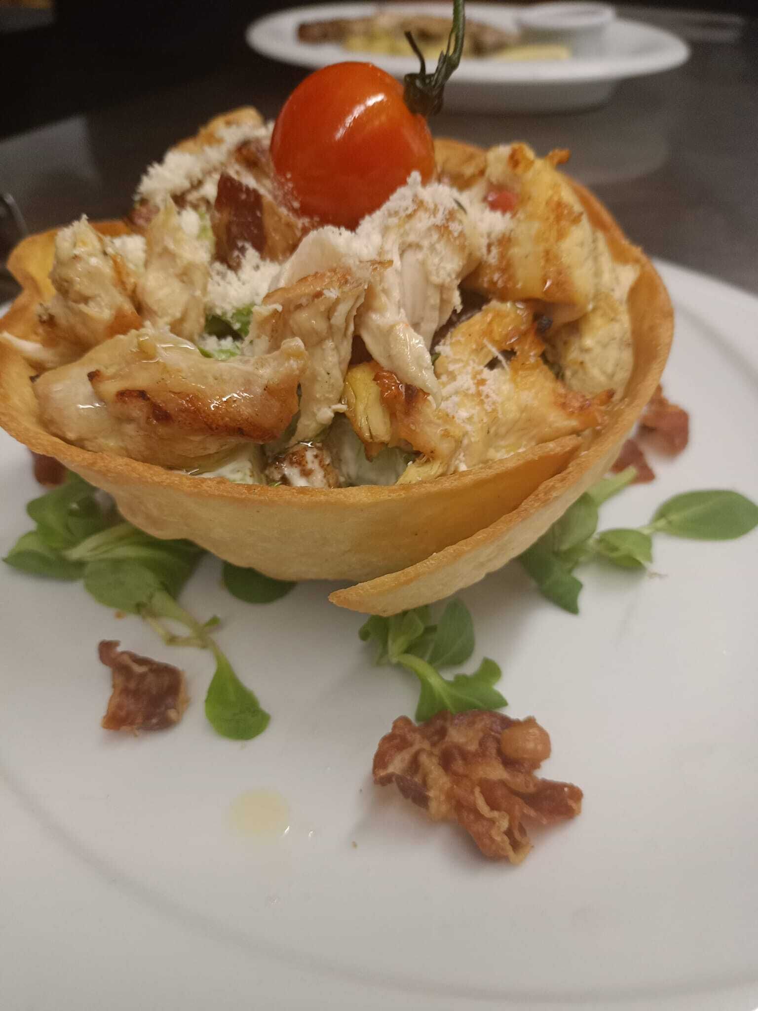 Un plato con un tomate cherry encima, rodeado de verduras y trocitos de tocino.