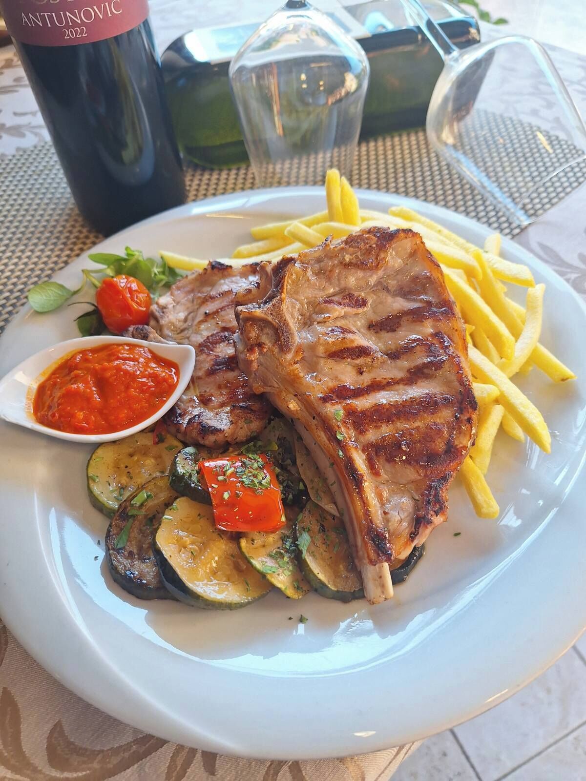 Ein Teller mit gegrilltem Steak, Pommes Frites, gegrilltem Gemüse und einer Beilage Soße.