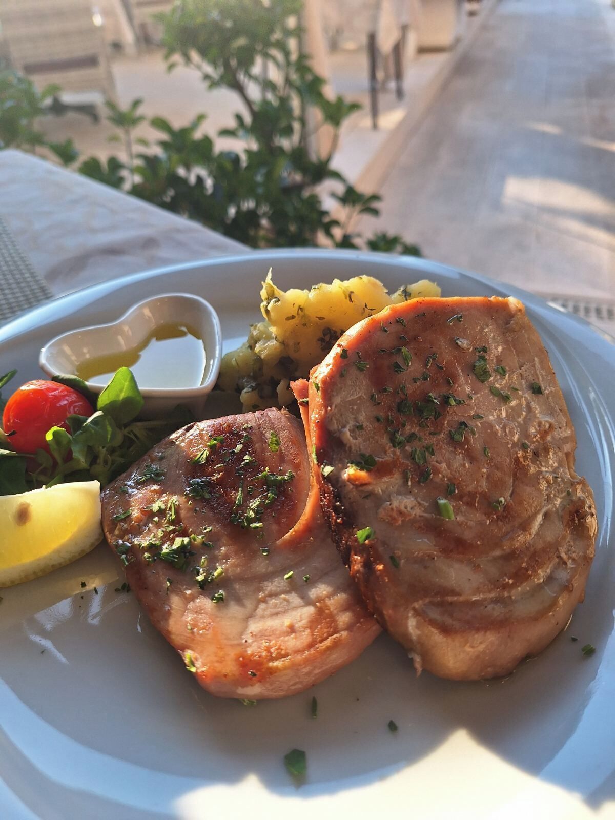 A plate with a slice of meat, potatoes, a cherry tomato, and a lemon wedge.