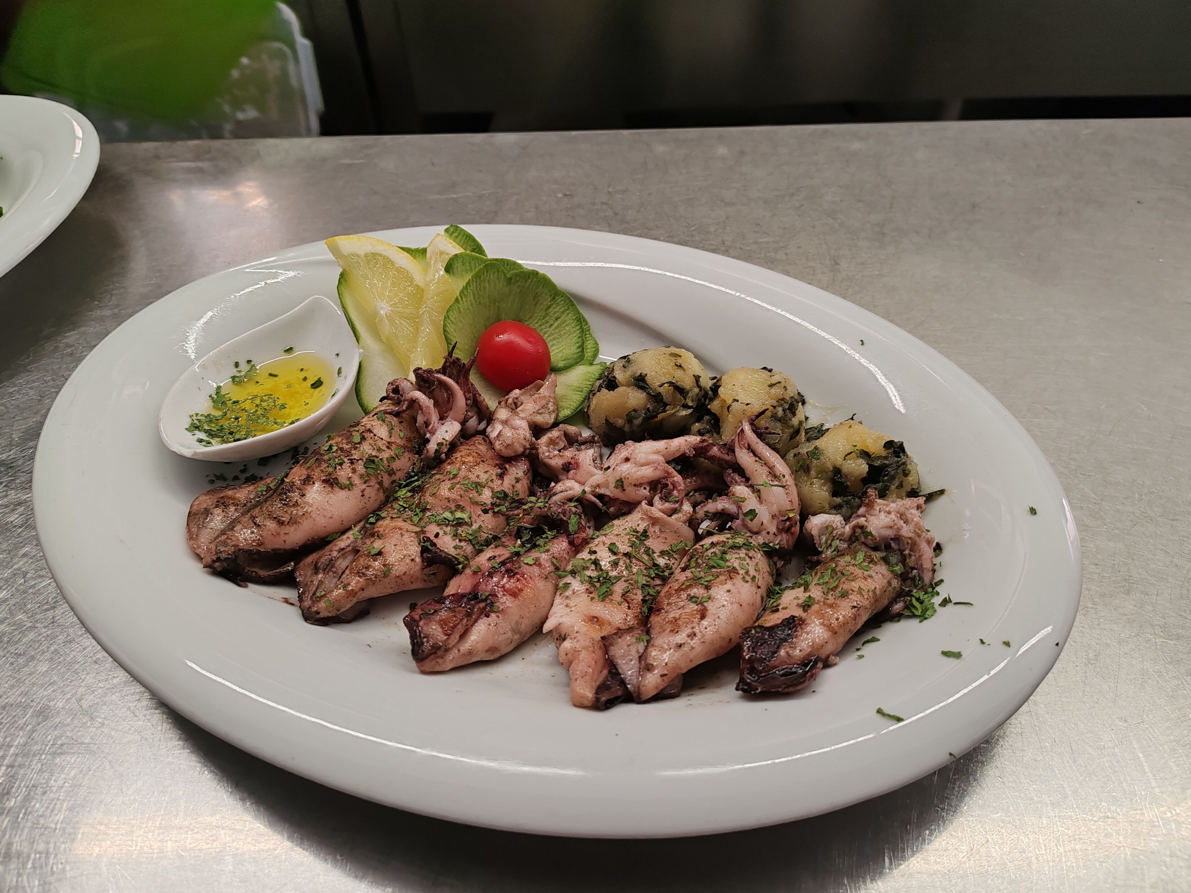 Un plato de pulpo a la parrilla con limón, aguacate y tomate cherry sobre un plato blanco.