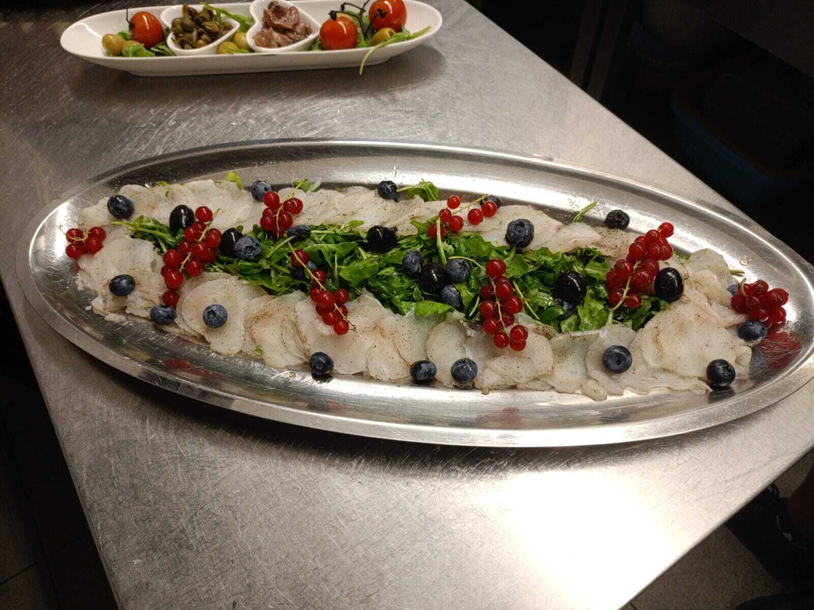 Eine Platte mit Fisch, Beeren und Grünzeug auf einer Metalltischplatte.