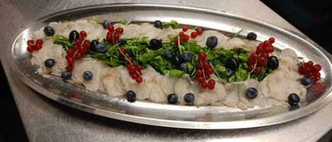 A platter of food with fish, berries, and greens on a metal table.