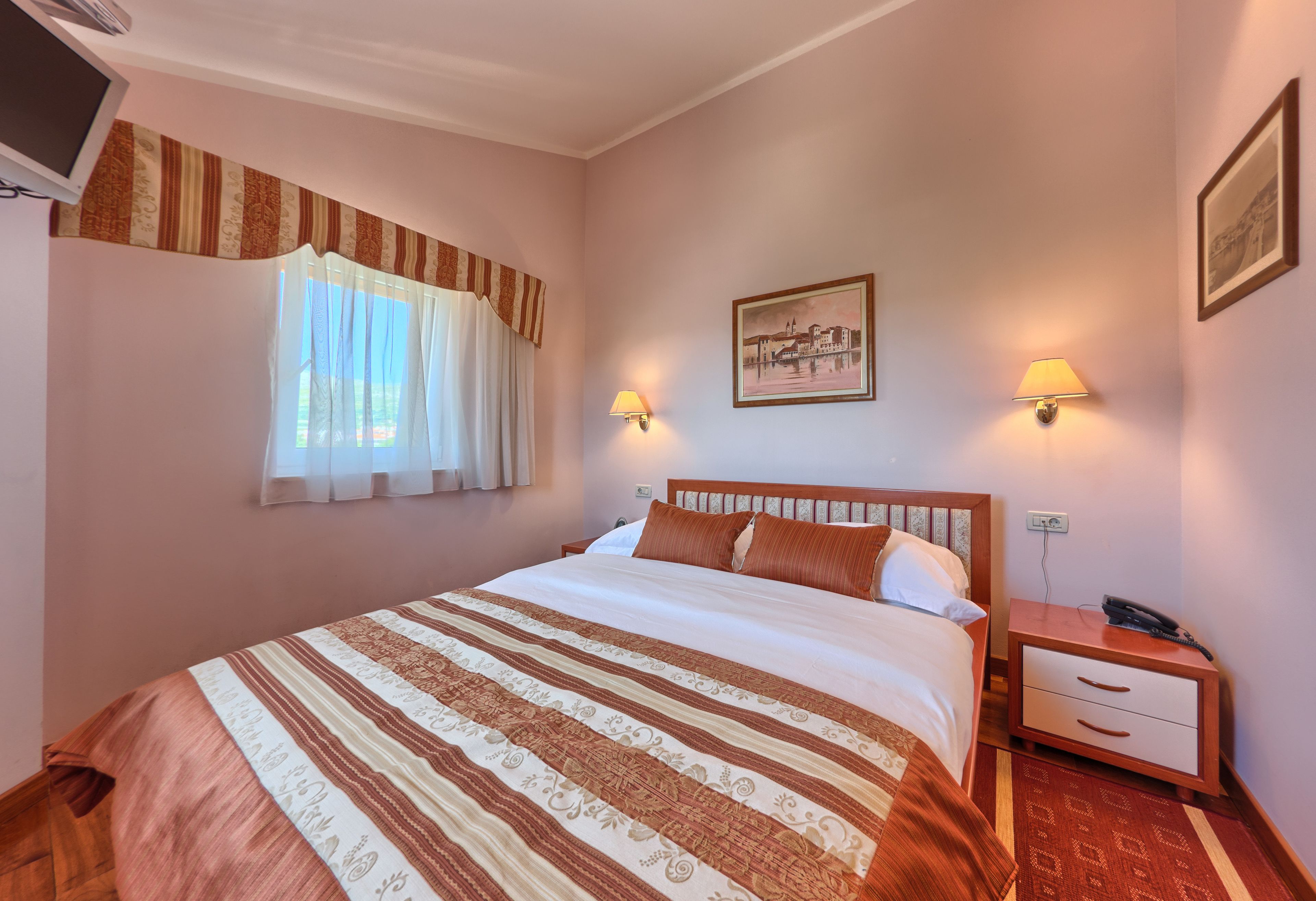 A neatly made bed with a striped bedspread, a nightstand with a lamp, and a framed picture on the wall.