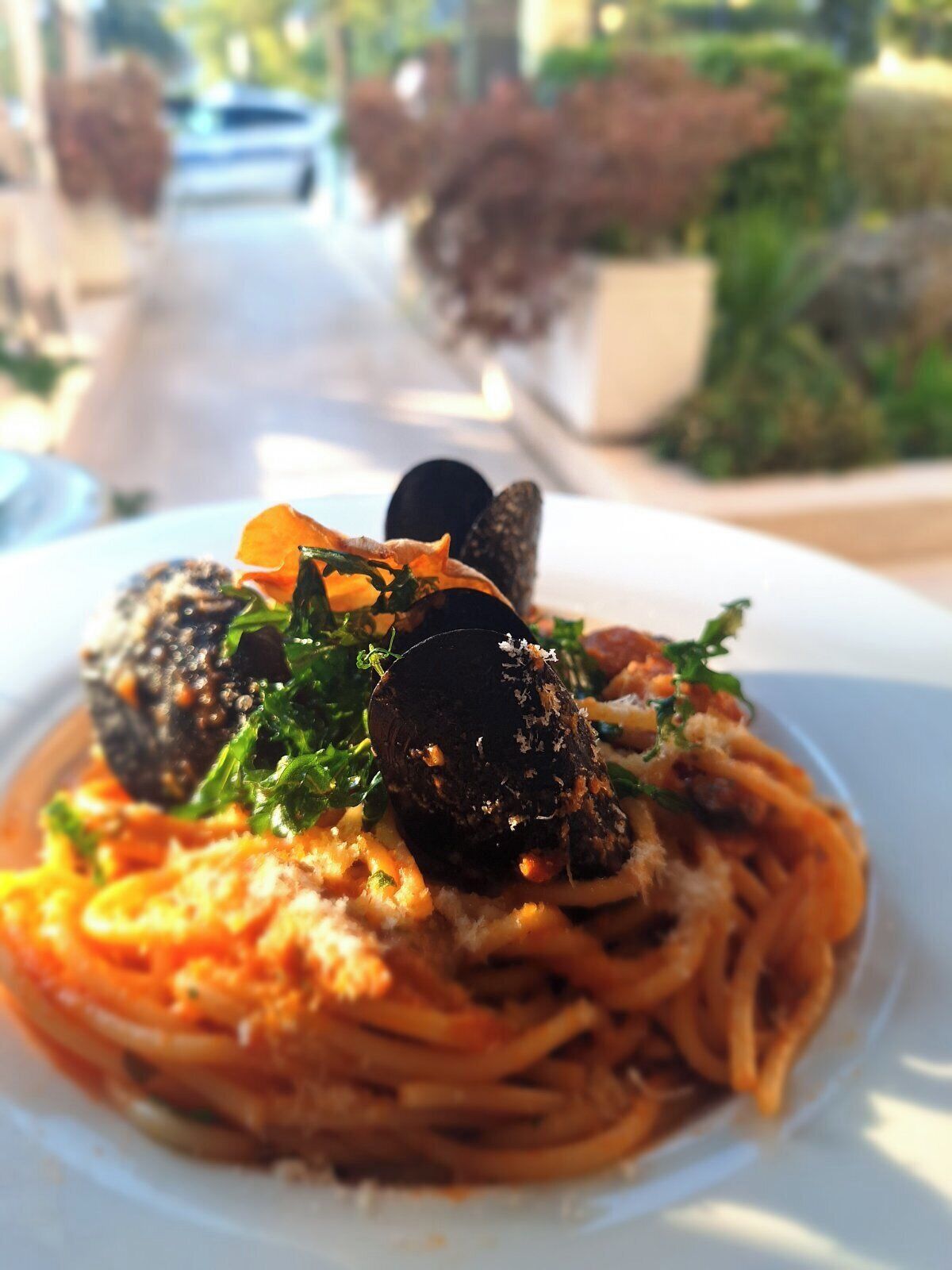 Un plato de espagueti con mejillones y vegetales verdes, servido en un plato blanco.