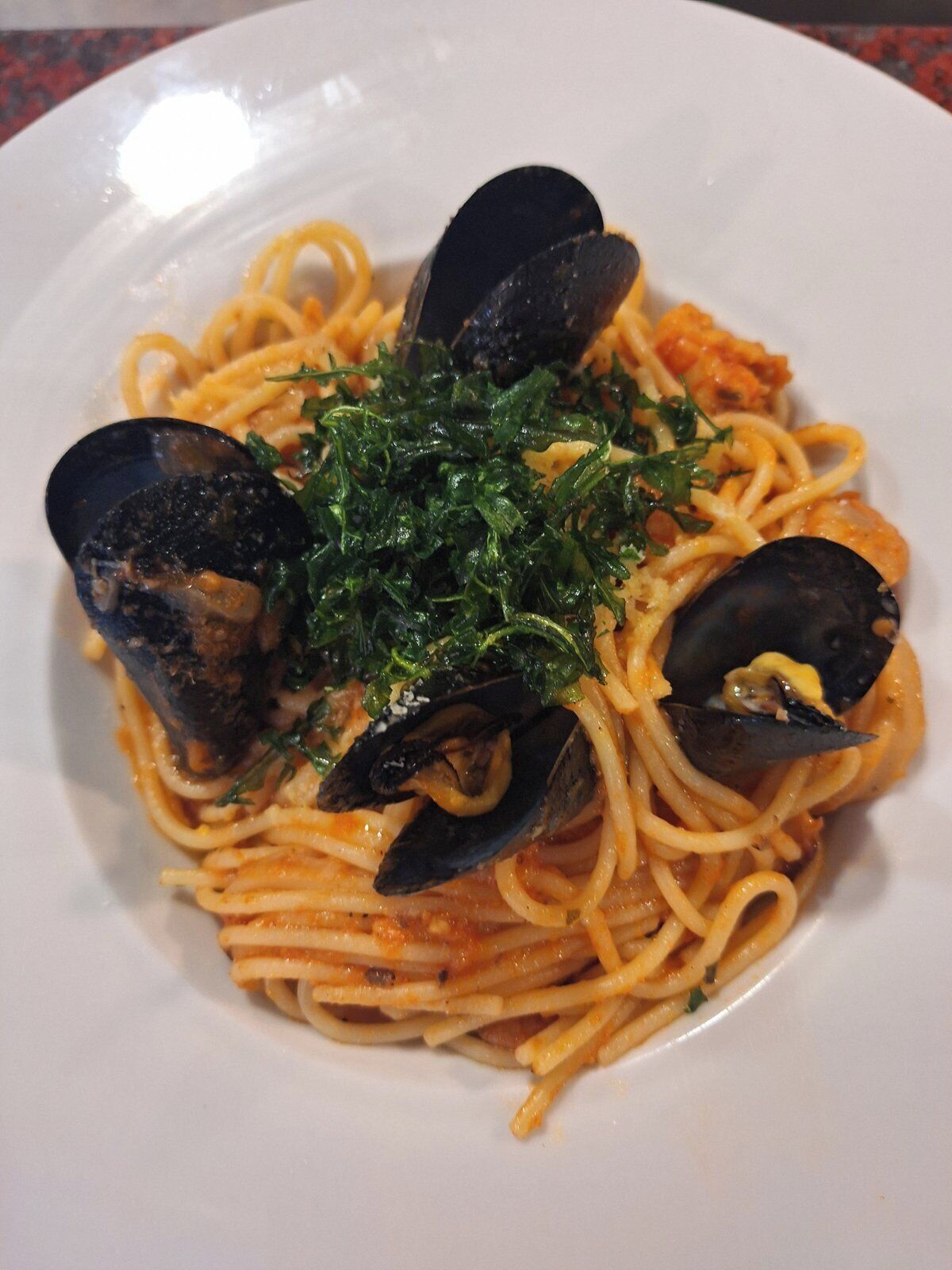 A plate of spaghetti with mussels and a garnish of green herbs.