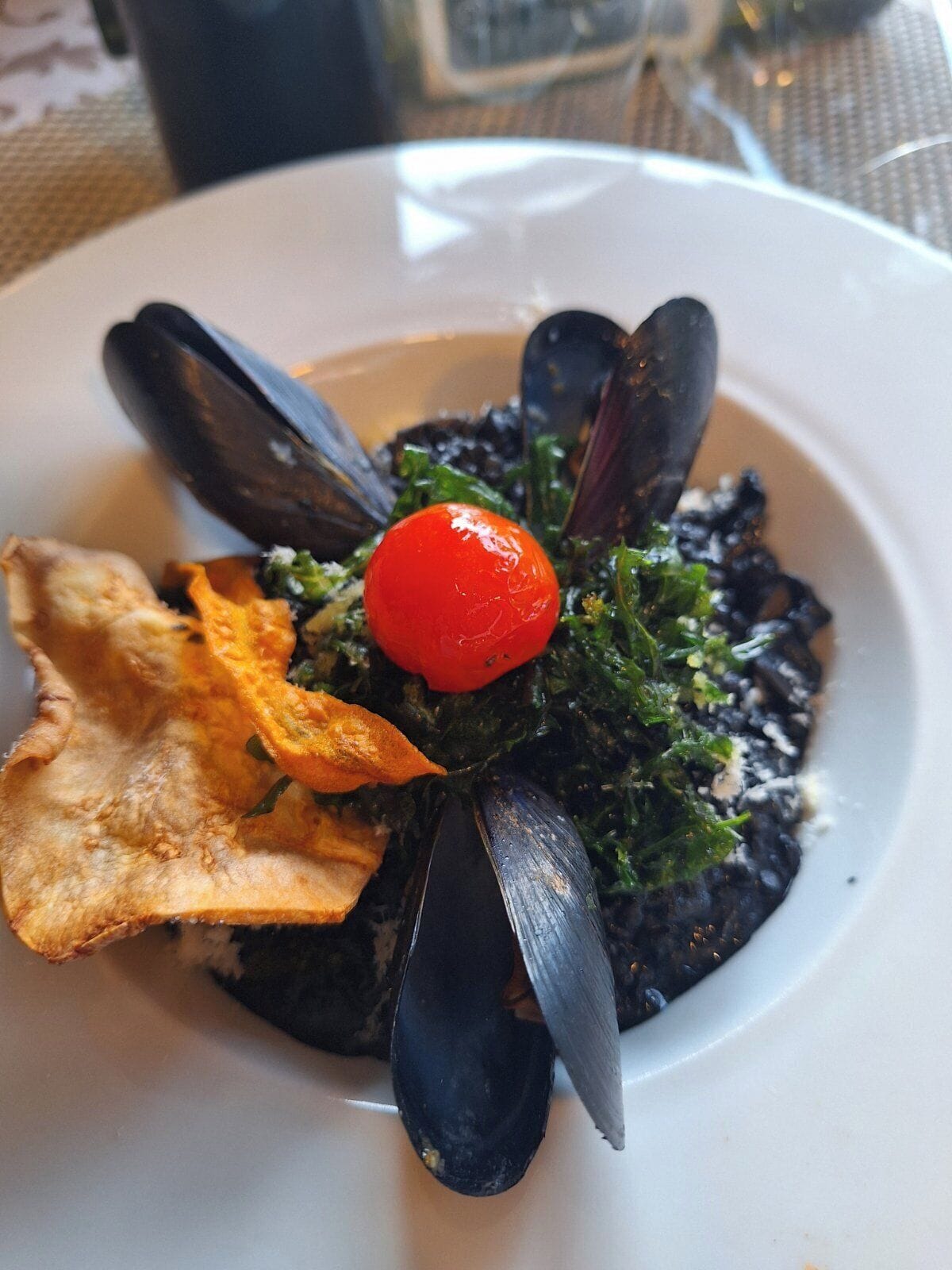 Un plato con mejillones, un tomate cherry y un trozo de comida frita.