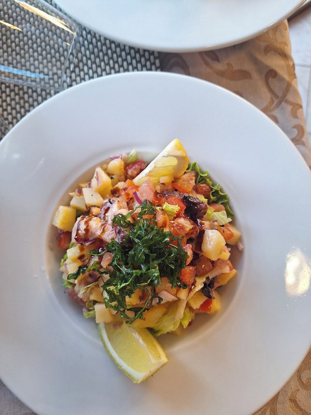 Un plato blanco con una ensalada, un gajo de limón y un trozo pequeño de lechuga.
