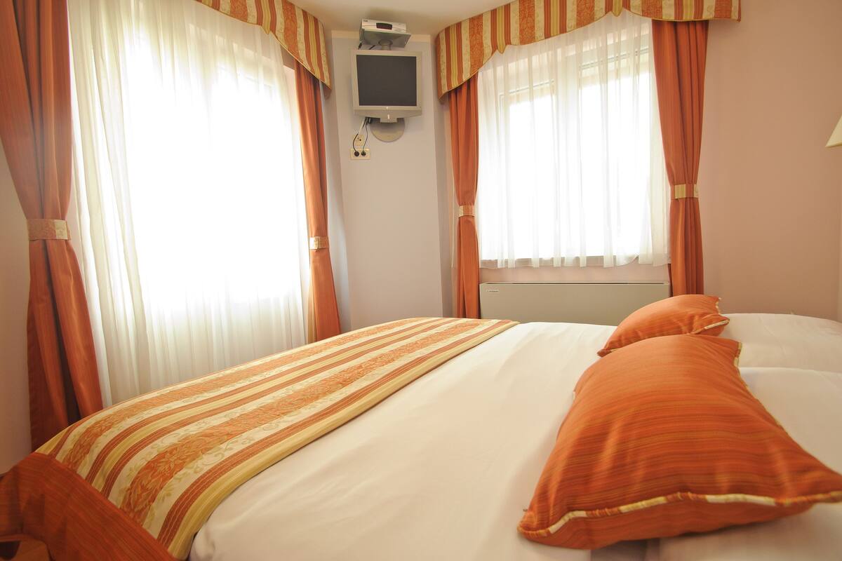 Una habitación de hotel con una cama, cortinas y un televisor fijado a la pared.