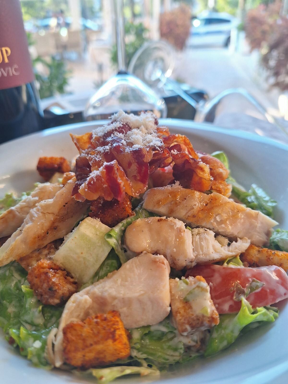 Salat mit Hähnchen, Speck und Croutons auf einem weißen Teller.