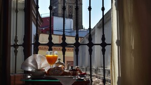 A dining table with a glass of orange juice and a plate of food, a window with a view of a building with a tower, and a curtain partially drawn. - Hotel Convento La Gloria (Seville)