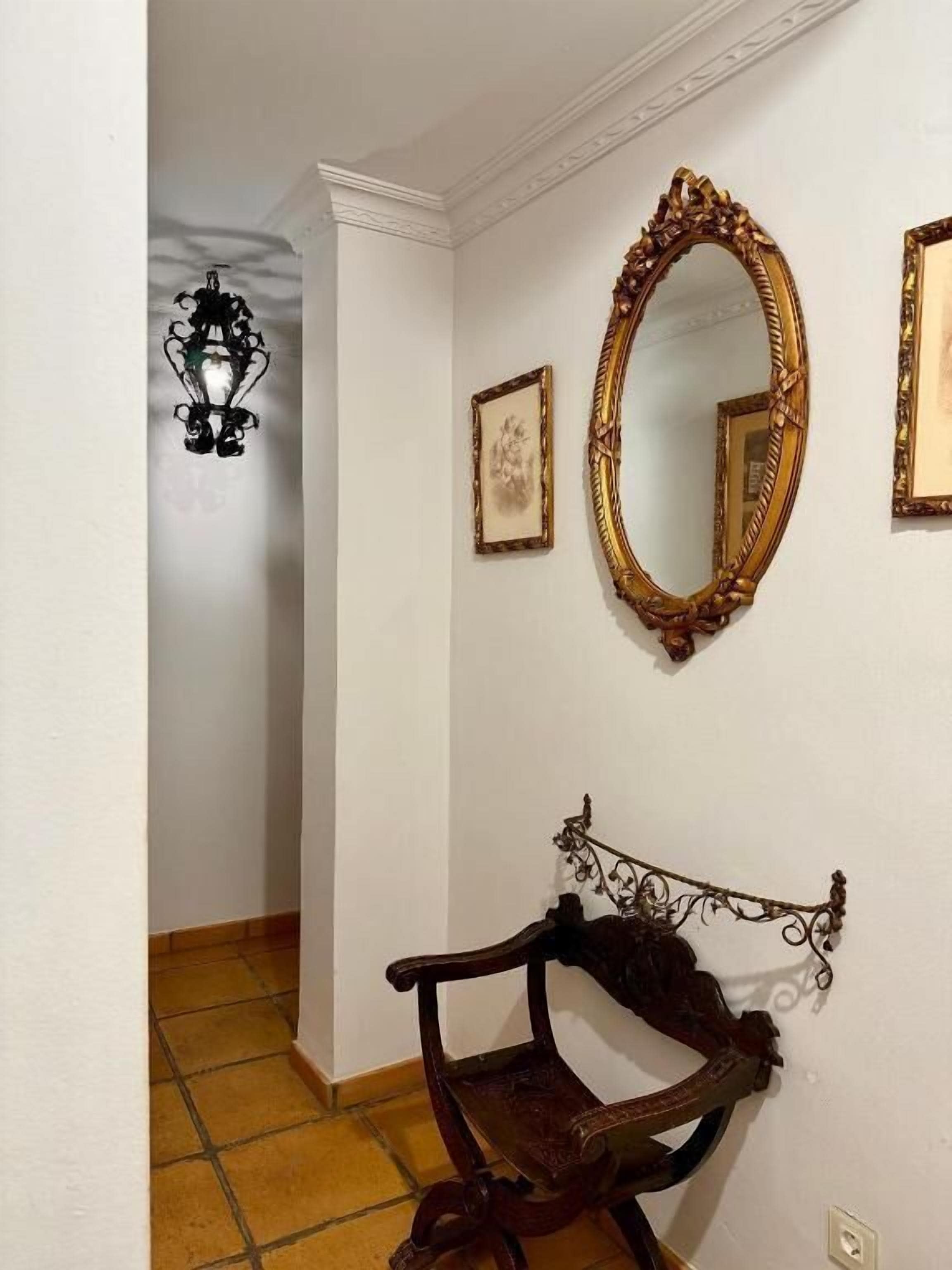 A hallway with a wooden bench, a large ornate mirror, and a wall-mounted light fixture.