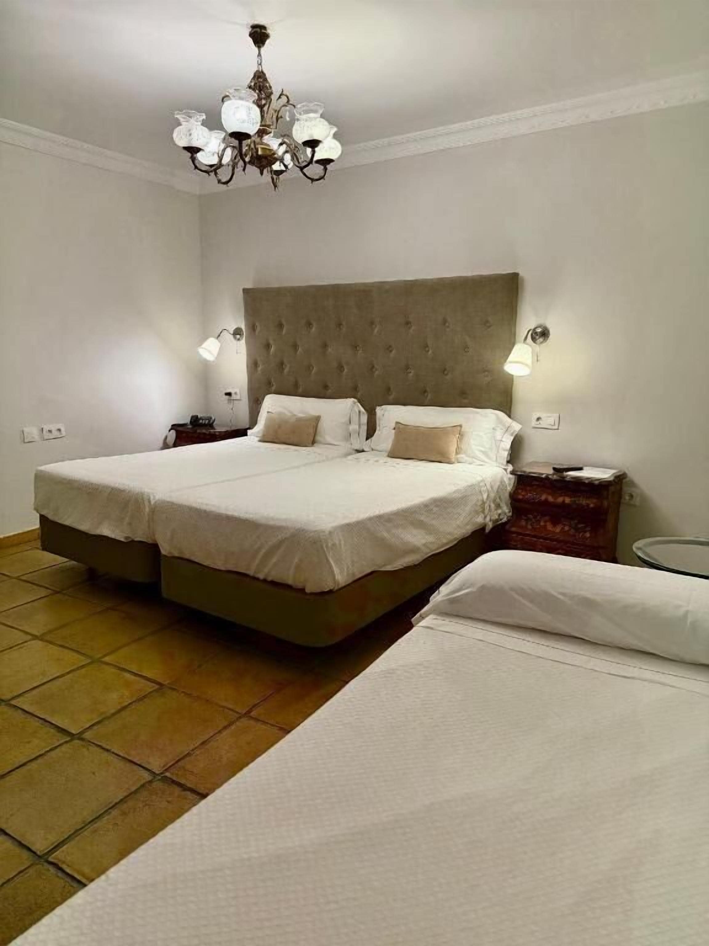 A bedroom with a large bed, a nightstand, a lamp, and a chandelier.