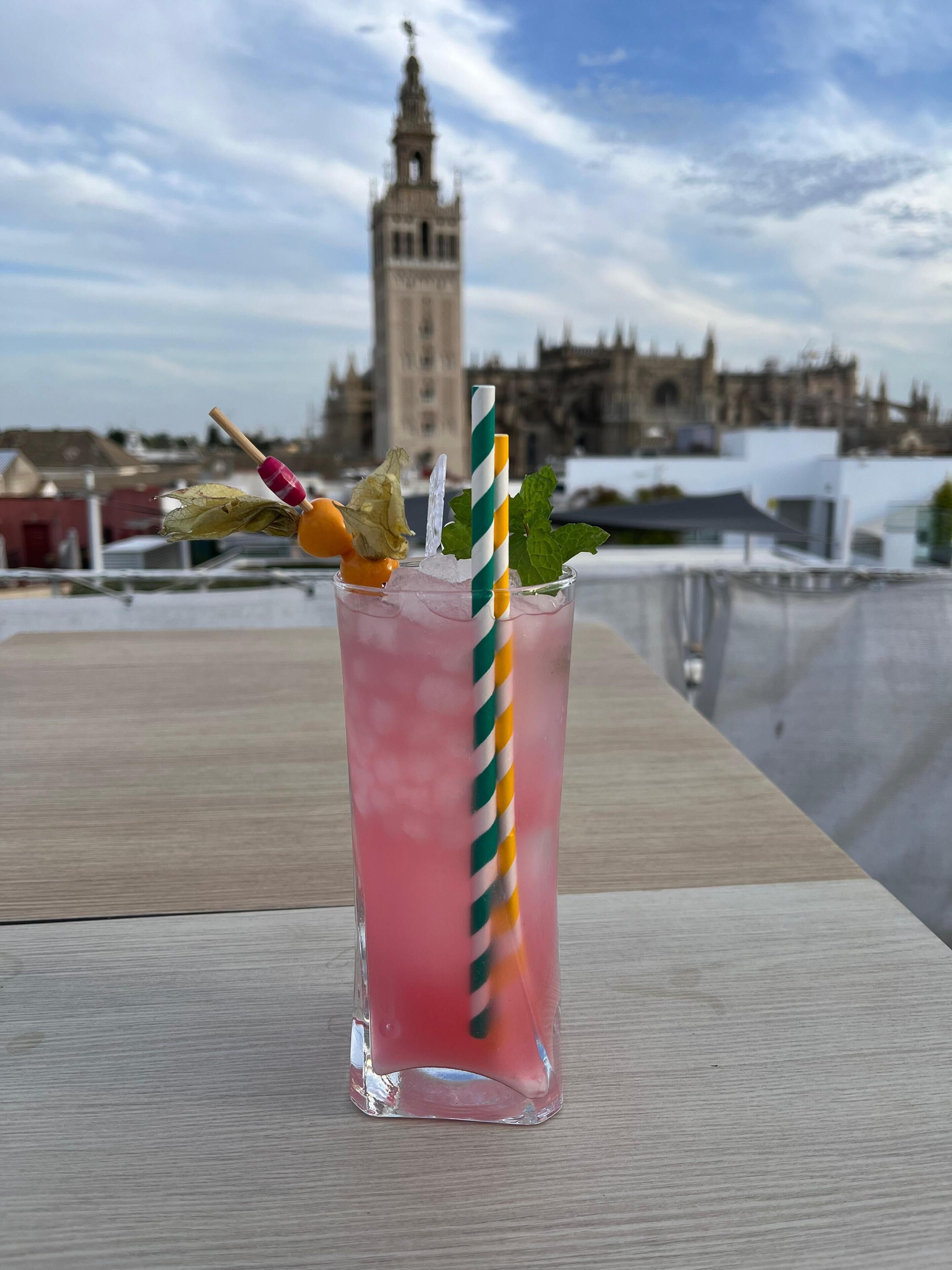 A cocktail with a striped straw and garnish on a table with a view of a historic building in the background.