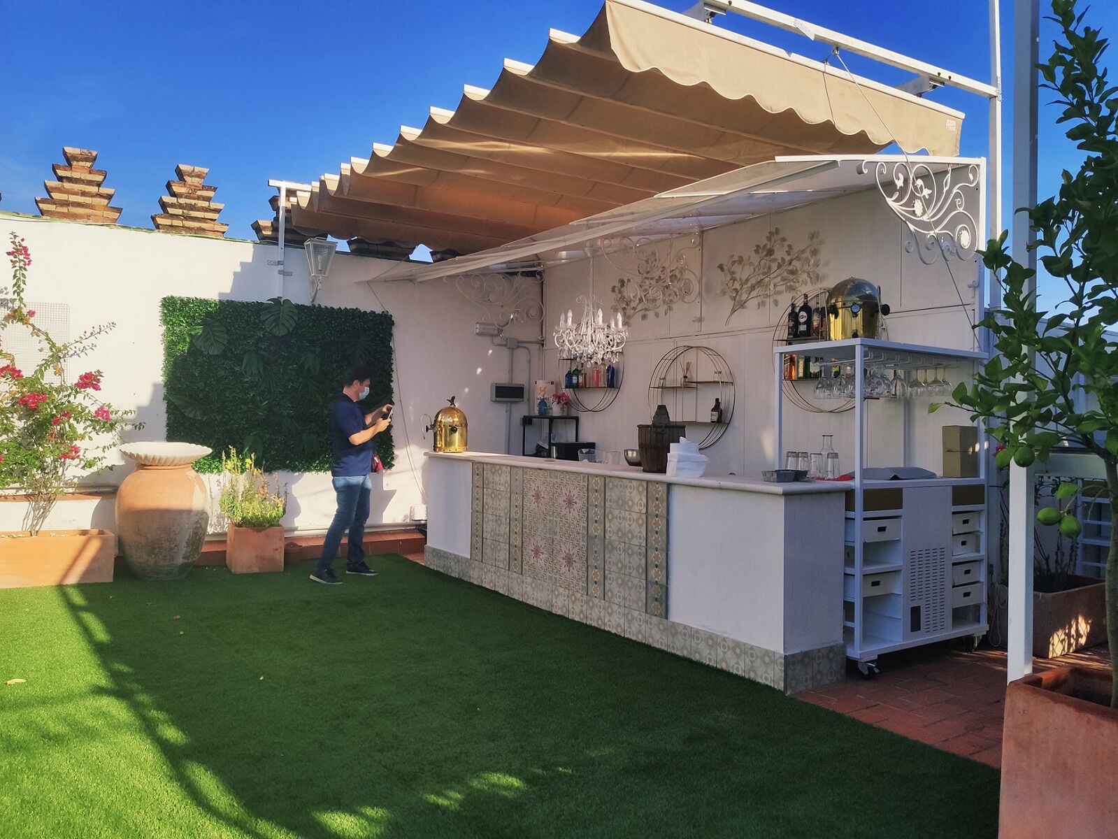 An outdoor bar area with a green lawn, a decorative wall, and a person standing near the bar.