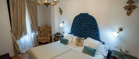 A bedroom with a large bed, two bedside tables, a chandelier, and a decorative wall piece.