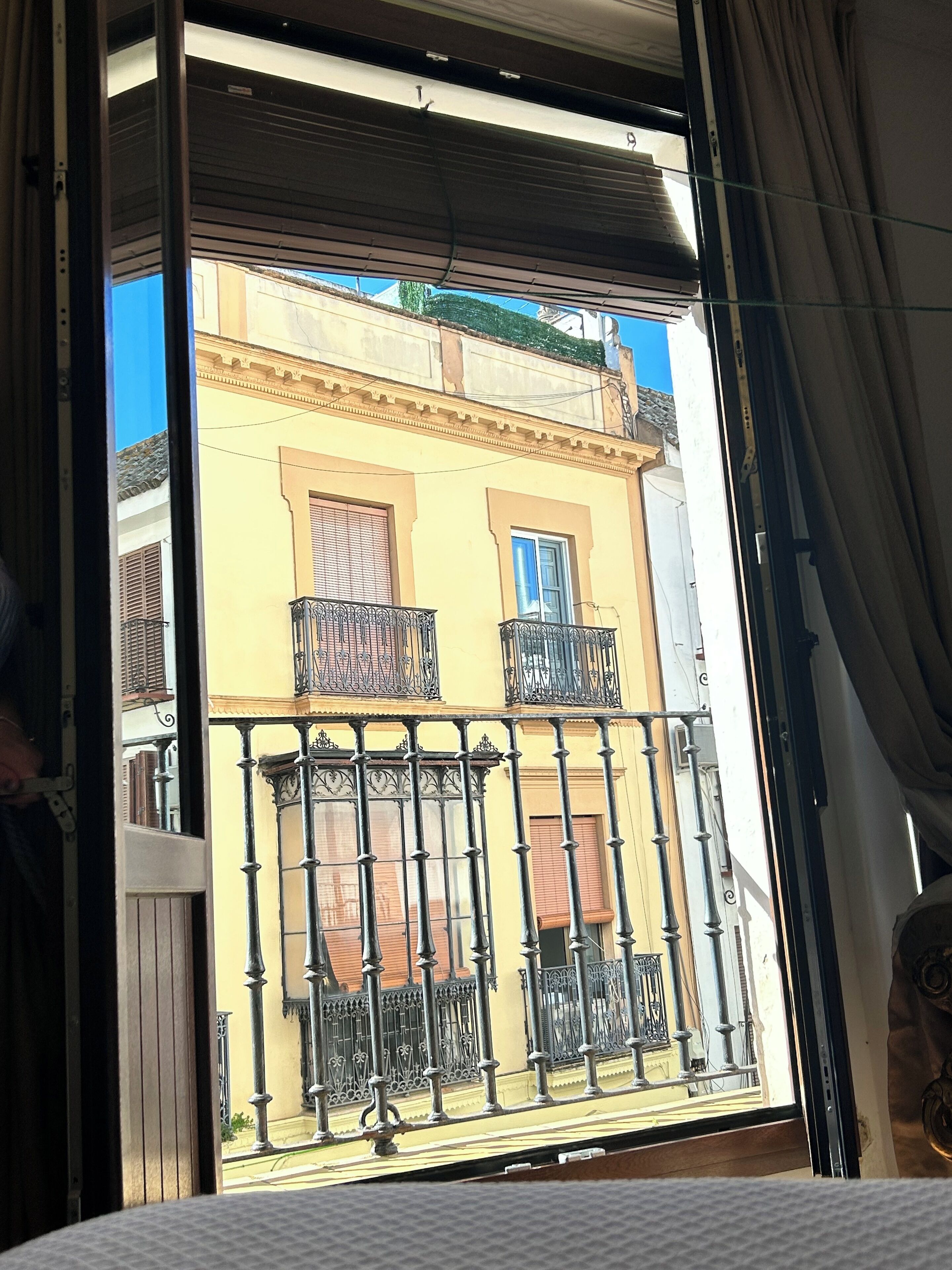 Une vue à travers une fenêtre donnant sur un balcon, avec en arrière-plan un immeuble à la façade jaune et une fenêtre bleue.