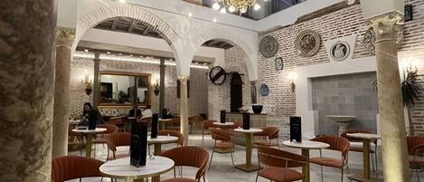 A spacious indoor area with multiple levels, featuring a central open space with tables and chairs, and a chandelier.