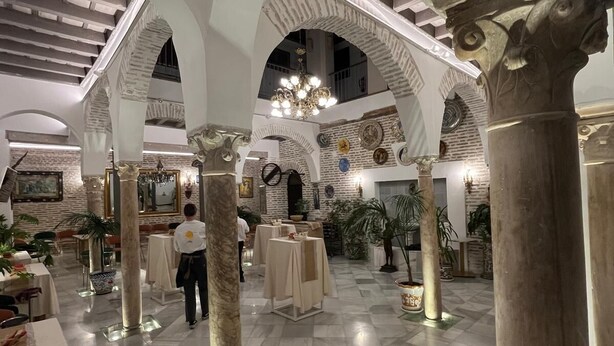 A spacious lobby with high ceilings, arched columns, and a chandelier. Tables and chairs are arranged for dining or socializing. - Hotel Convento La Gloria (Seville)