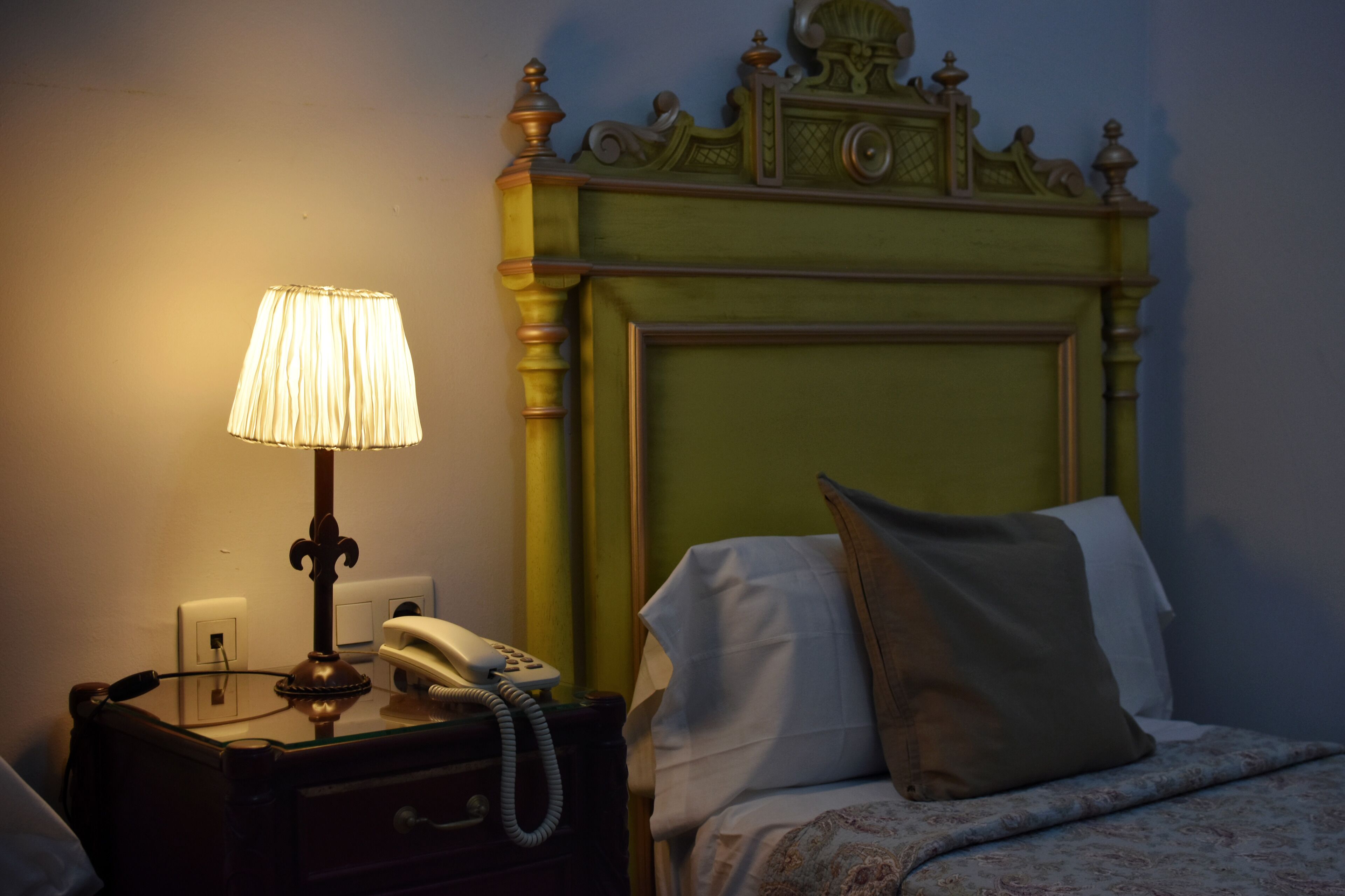 A neatly made bed with a green headboard, a bedside lamp, and a telephone on a nightstand.