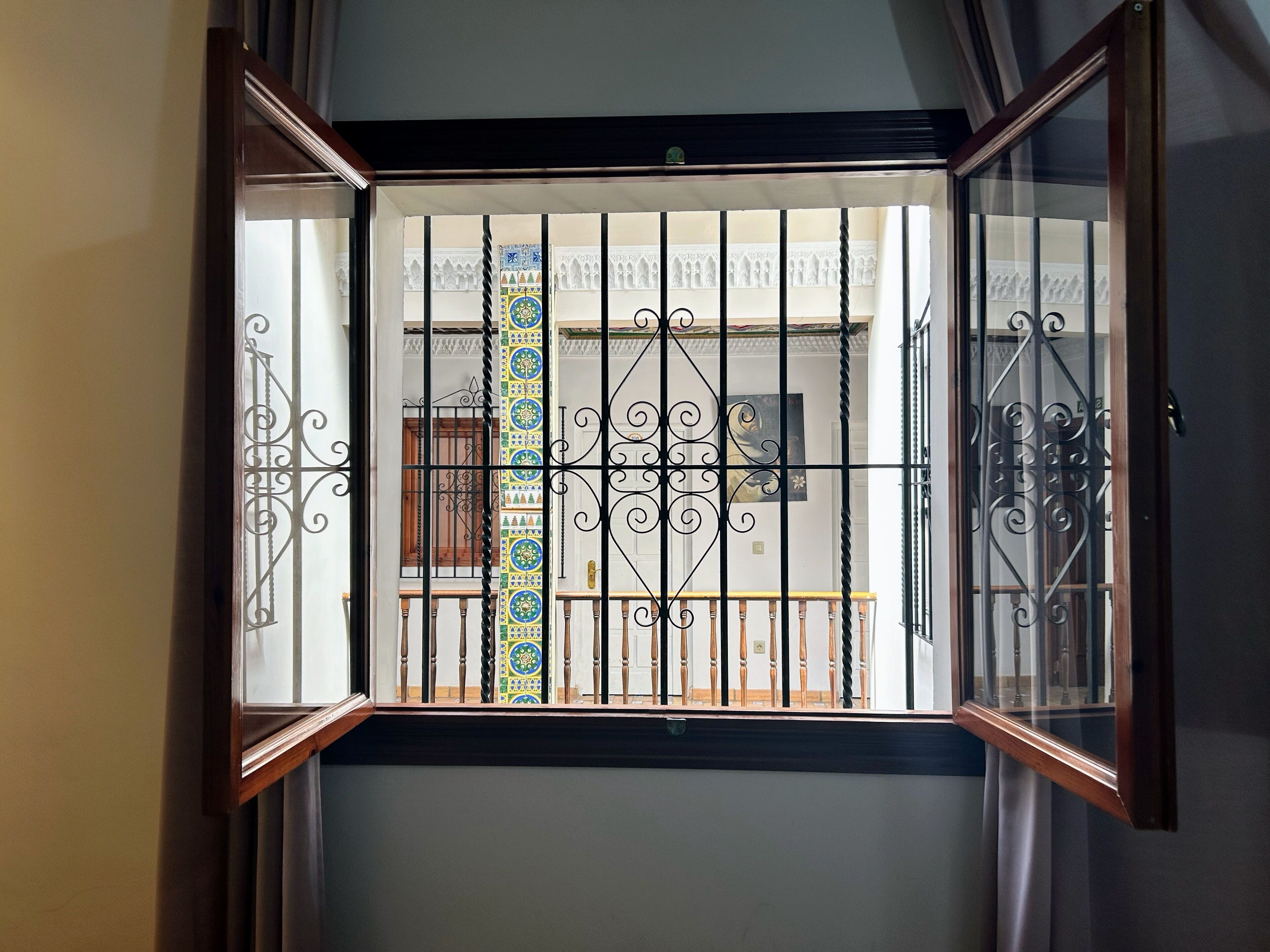 A view through a window with decorative iron bars and a patterned curtain.