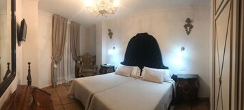 A hotel room with a large bed, two bedside tables, a chandelier, and a classic chair.
