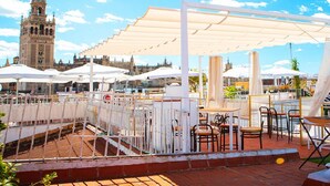 An outdoor seating area with tables and chairs under a canopy, overlooking a historic building with a tower. - Hotel Convento La Gloria (Seville)