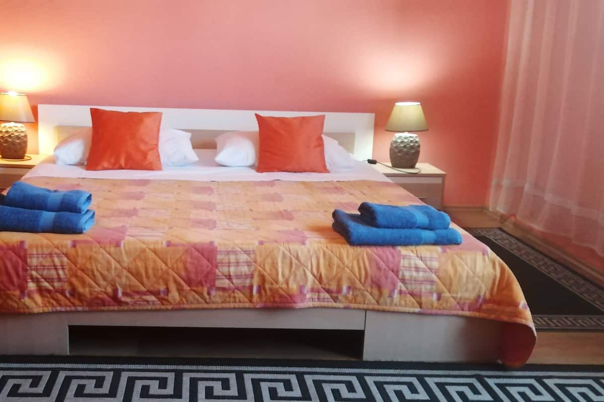 Habitación de hotel con una cama, dos mesitas de noche, un florero con plantas secas y una alfombra estampada.