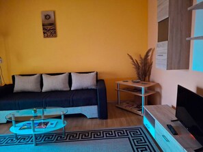 A living room with a sofa, a glass coffee table, a TV stand, and a wall-mounted artwork. - Villa Luketa (Podstrana)