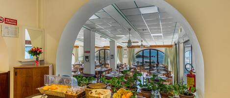 Un comedor con una mesa de buffet, plantas en macetas y vistas a través de un arco.