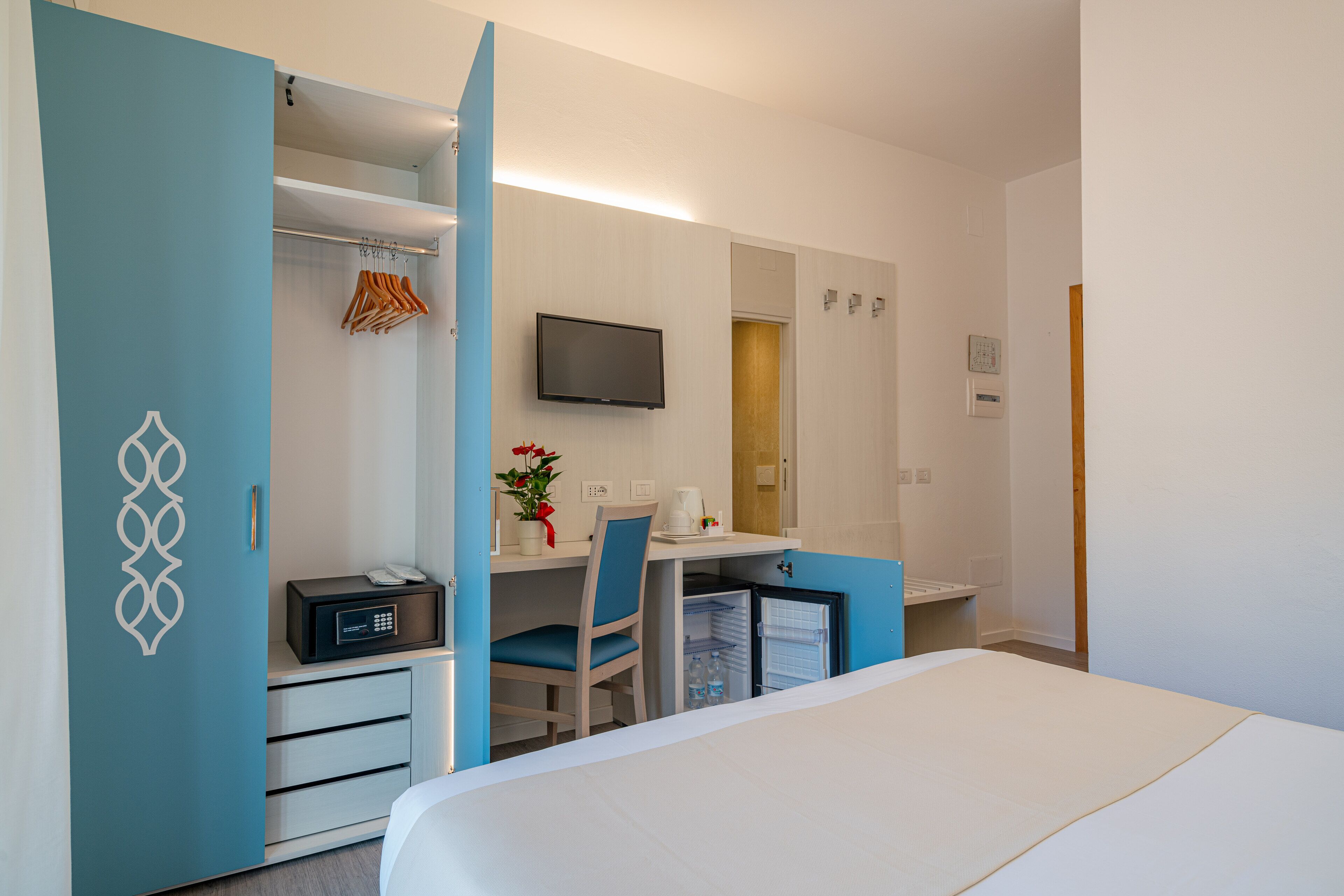 A hotel room with a bed, a desk with a chair, a television, and a wardrobe.