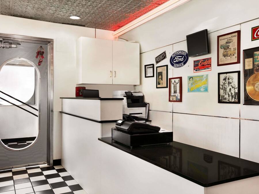 A kitchen with white cabinets, a black countertop, and a checkered floor. There are framed pictures and memorabilia on the wall.