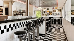 Un restaurant de style rétro avec un sol à carreaux, des tabourets de bar et un comptoir où est affiché le menu.
