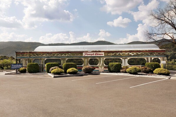 A diner with a covered roof, surrounded by neatly trimmed bushes and a parking lot.