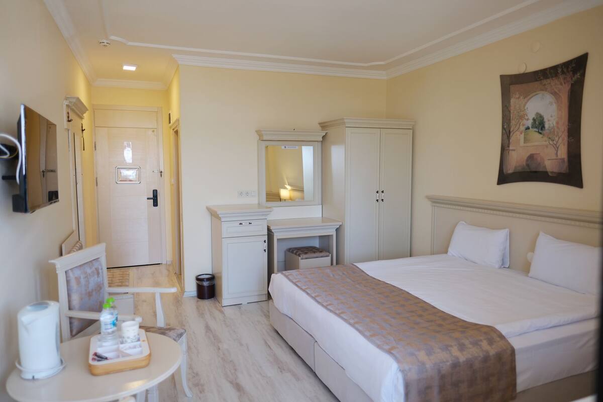 Une chambre d’hôtel avec un lit, un bureau doté d’un miroir, une armoire et un tableau au mur.