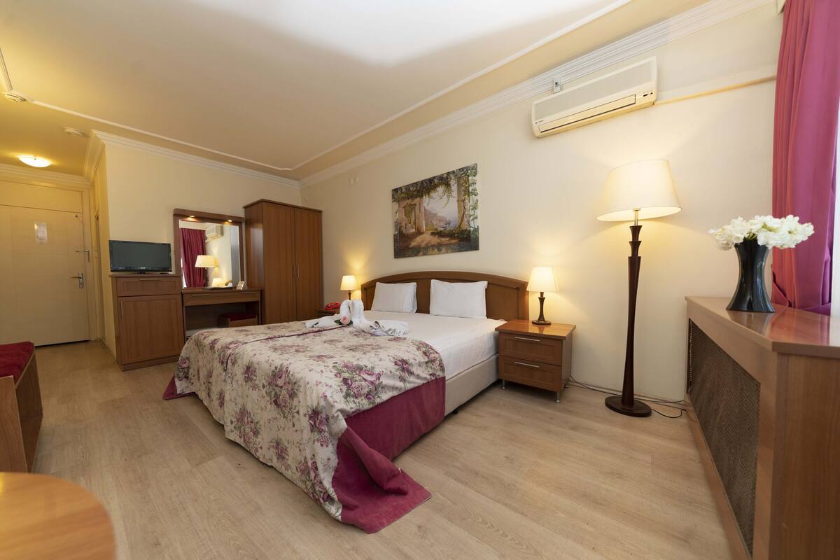 Une chambre d’hôtel comprenant un lit, des tables de chevet, un bureau, une chaise, une télévision, une armoire et un tableau au mur.