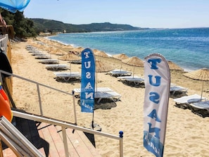 En strand med parasoller og liggestole, samt flag med teksten "TUGA".