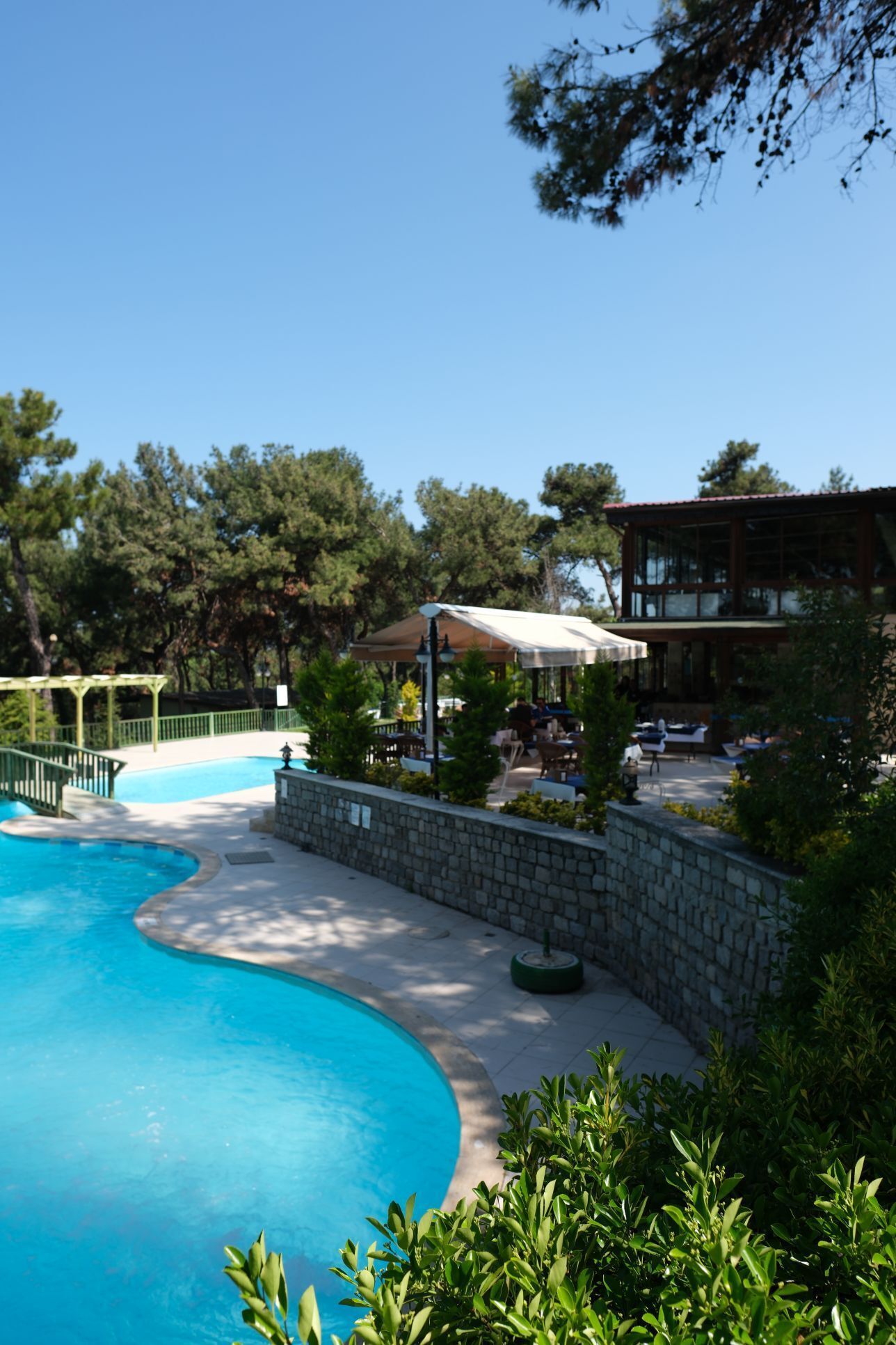 A swimming pool with a stone wall and a covered seating area with tables and chairs.