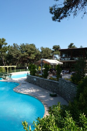 A swimming pool with a stone wall and a covered seating area with tables and chairs.