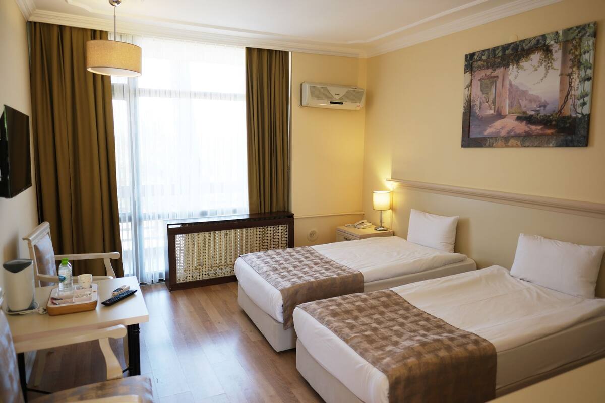 Une chambre d’hôtel avec deux lits, un bureau avec une lampe, un tableau au mur et un appareil de climatisation.
