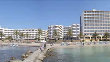 A coastal hotel with multiple floors, a beach in the foreground, and palm trees.