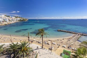 A beach with clear turquoise water, a sandy shore, and a few boats in the distance. - Hotel Ibiza Playa (Ibiza Town)