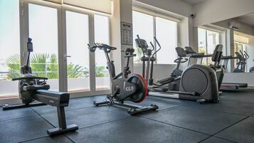 Een sportschool met cardioapparatuur, grote ramen en uitzicht op palmbomen.