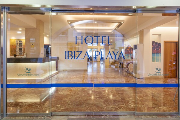 Un vestíbulo de hotel con un mostrador de recepción, una franja azul y un letrero que dice "HOTEL IBIZA PLAYA".