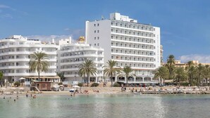 A beachfront hotel with multiple white buildings, palm trees, and a clear blue sky. - Hotel Ibiza Playa (Ibiza Town)