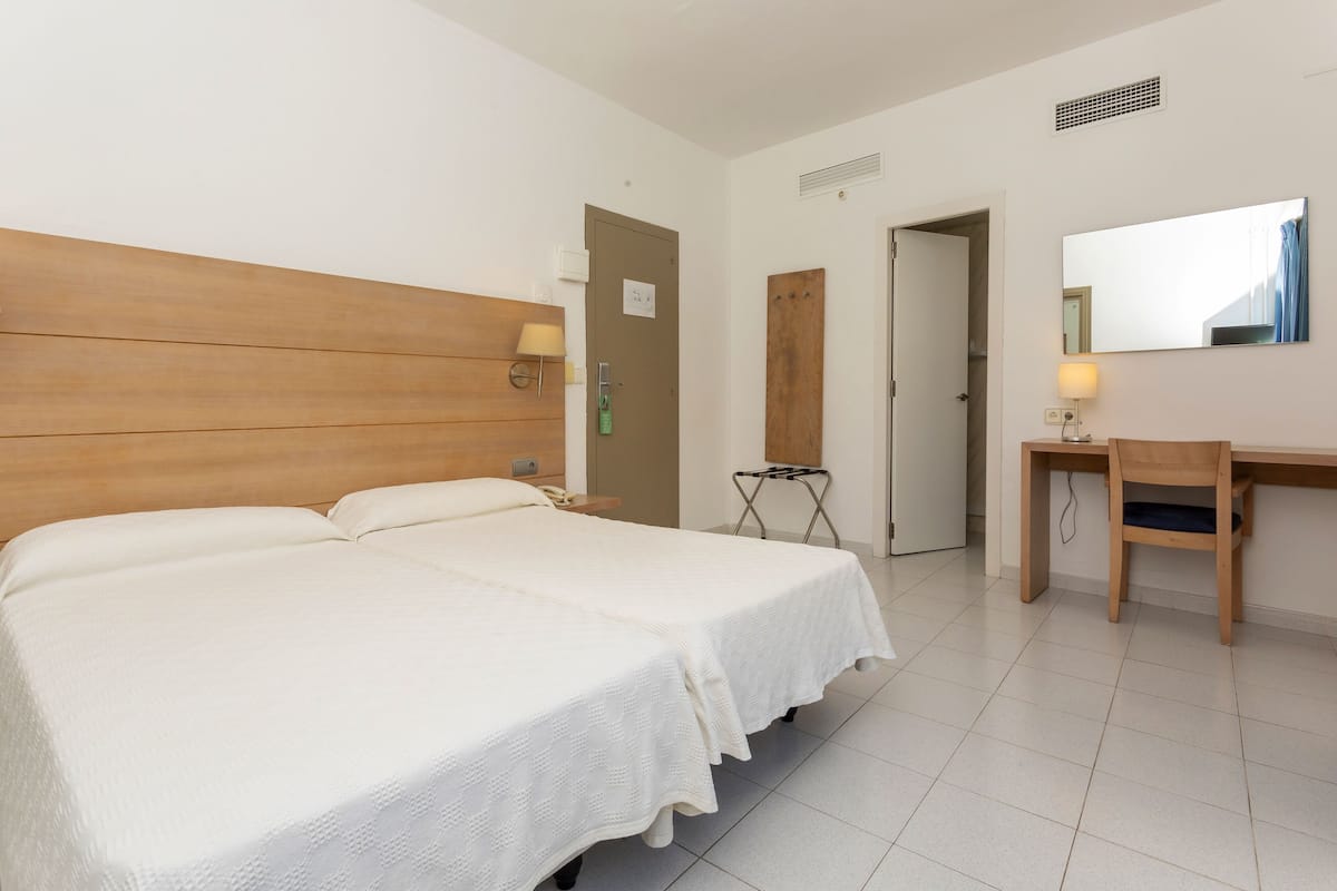 Una habitación de hotel con dos camas, un escritorio, una silla, un espejo y una puerta.