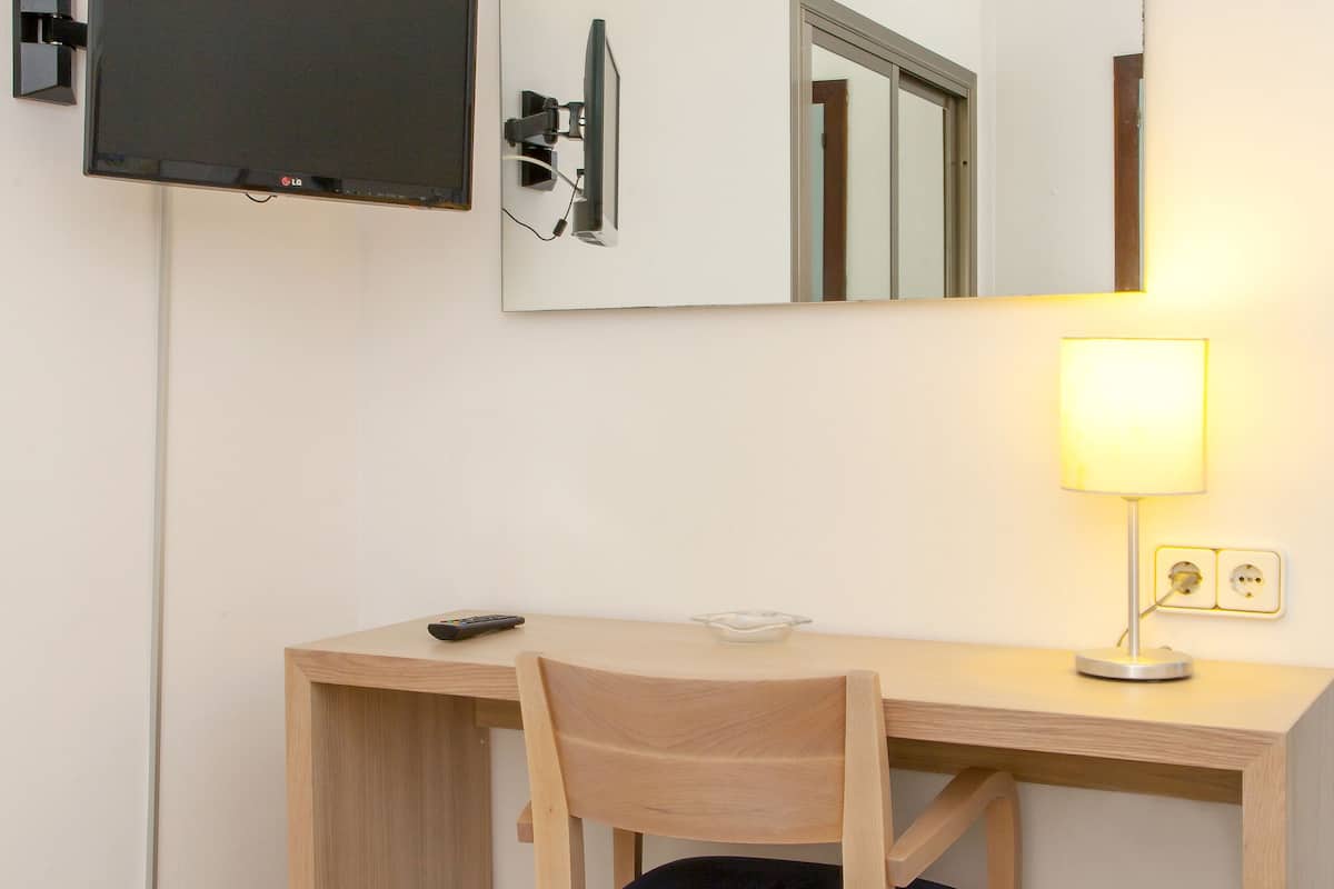 Habitación de hotel con un escritorio de madera, una silla, un televisor montado en la pared y una lámpara de noche.