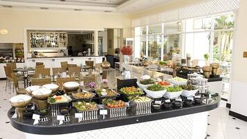 A buffet area with various food stations, a bar in the background, and a view of the outdoors through large windows.