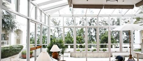 A spacious indoor area with large windows, wicker furniture, and a ceiling fan.