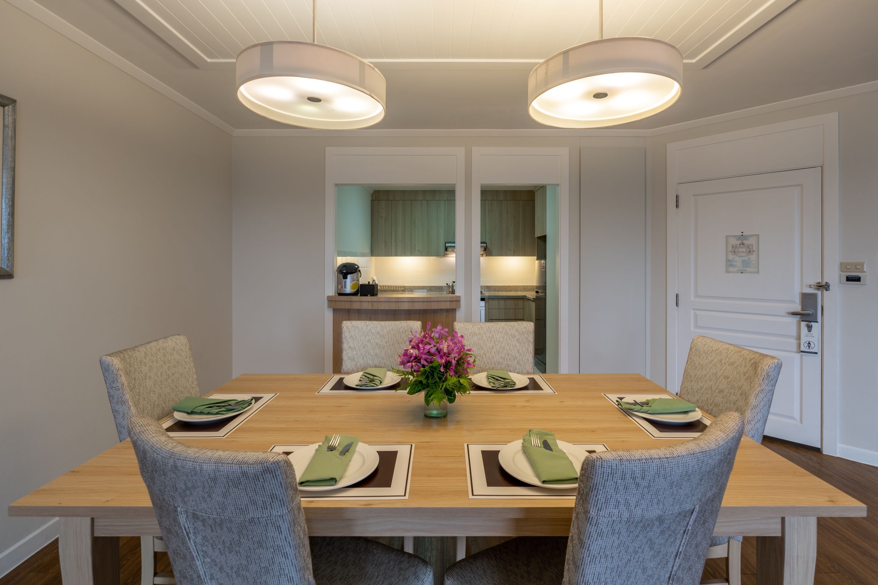 Une salle à manger avec une table en bois dressée pour quatre personnes, entourée de chaises rembourrées.